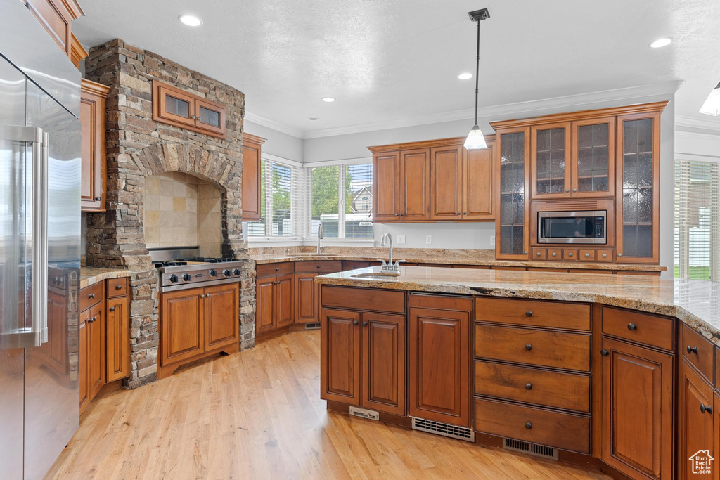 Kitchen featuring brown cabinets, appliances with stainless steel finishes, ornamental molding, and a sink