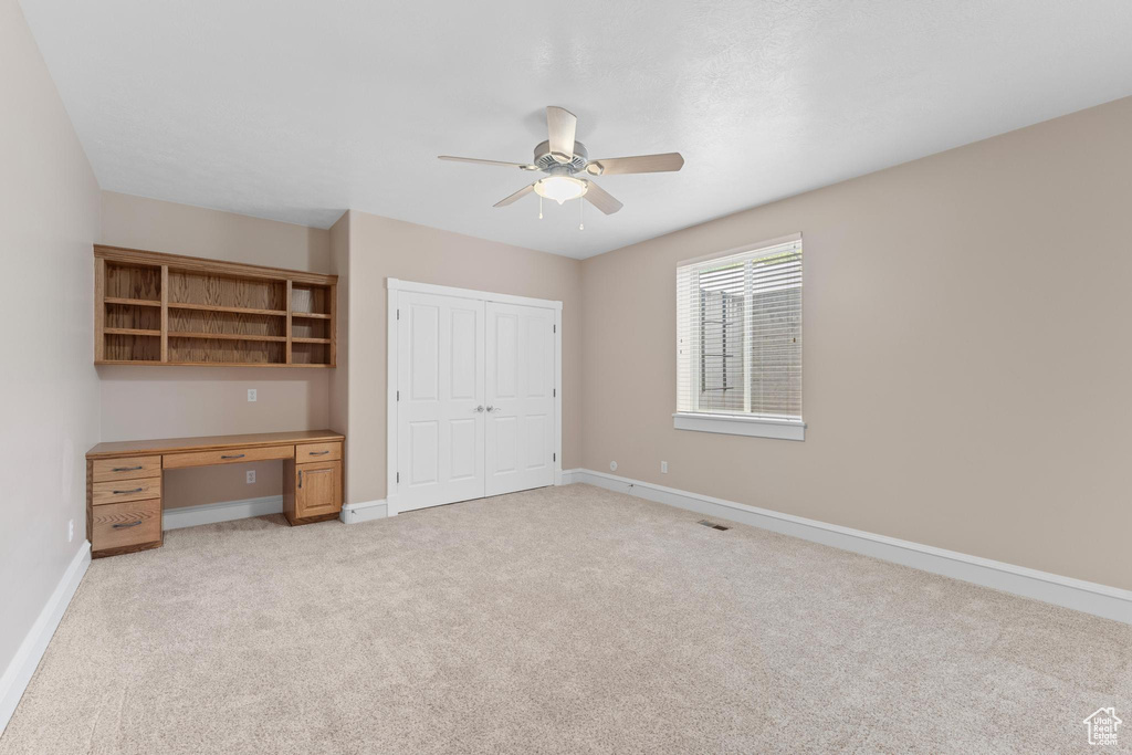 Unfurnished bedroom with ceiling fan, light carpet, built in desk, baseboards, and a closet