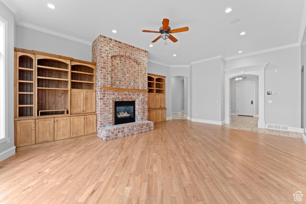 Unfurnished living room featuring ceiling fan, a fireplace, light wood-style floors, arched walkways, and visible vents