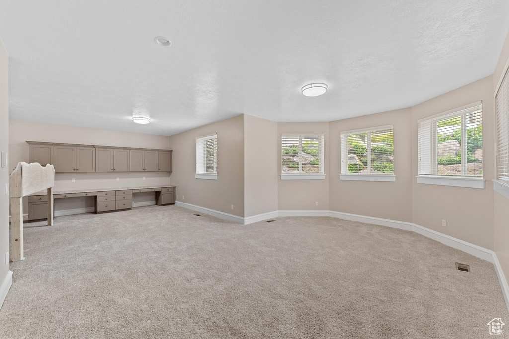 Unfurnished living room with baseboards, light colored carpet, built in desk, and visible vents