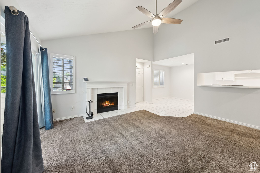 Unfurnished living room with ceiling fan, visible vents, a tiled fireplace, and a wealth of natural light