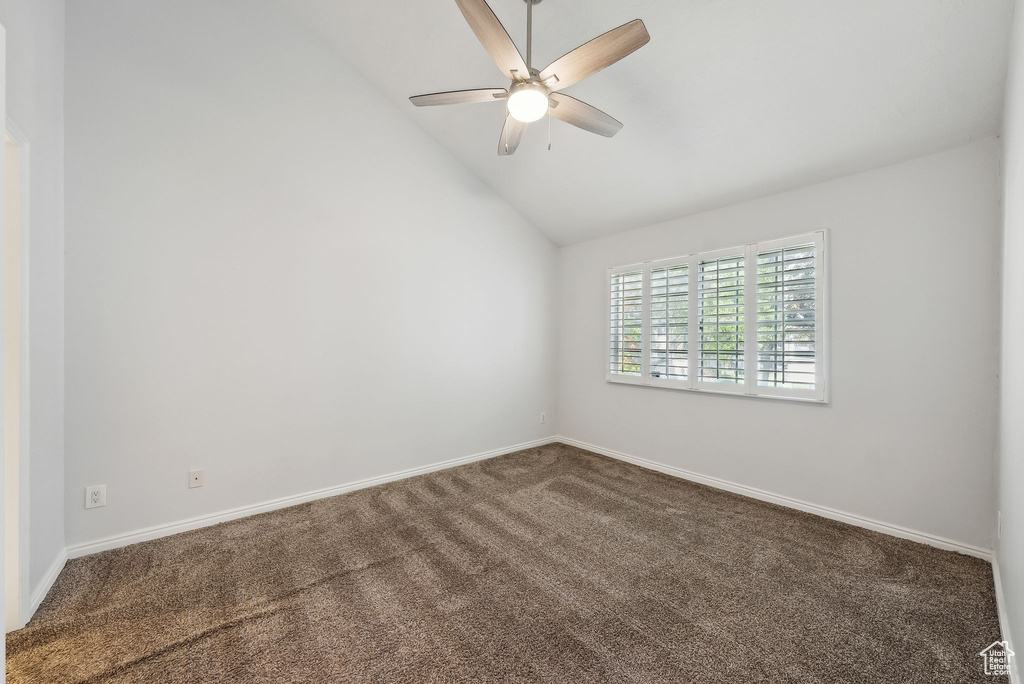 Carpeted spare room featuring baseboards, ceiling fan, and vaulted ceiling