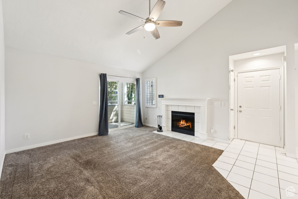 Unfurnished living room with a ceiling fan, a tiled fireplace, tile patterned flooring, high vaulted ceiling, and baseboards