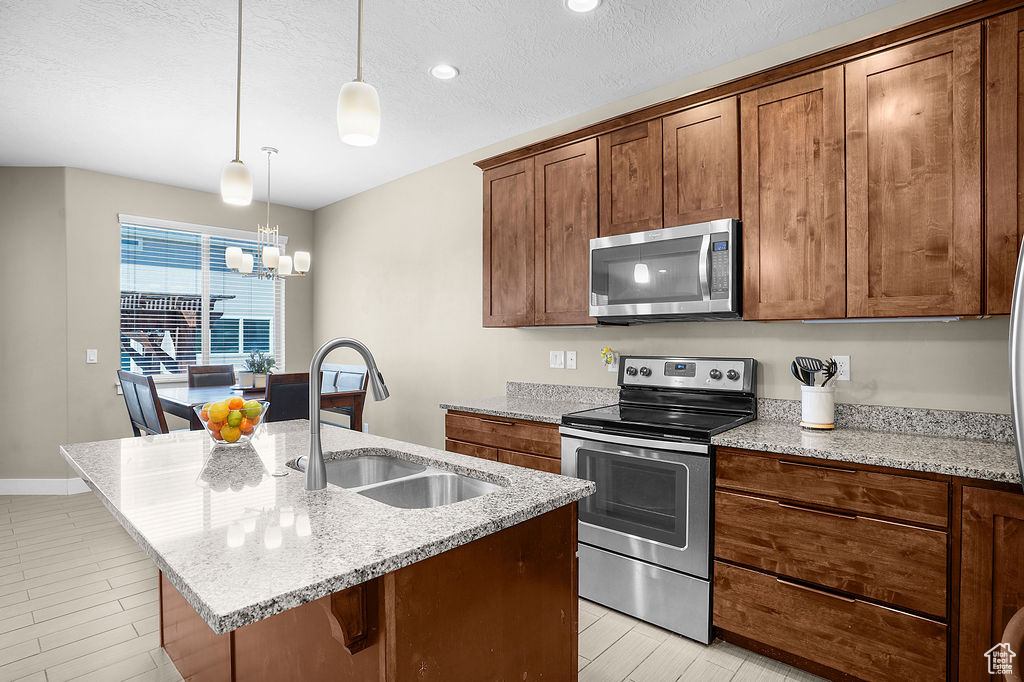 Kitchen with light stone counters, a sink, a chandelier, an island with sink, and stainless steel appliances