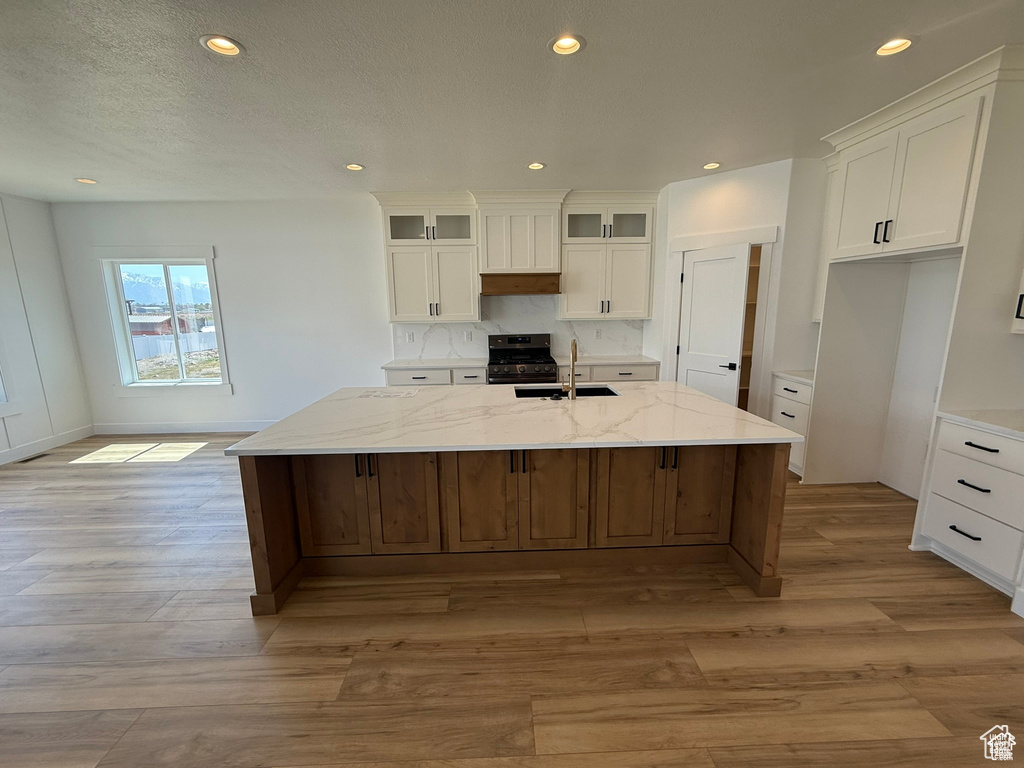 Kitchen featuring a sink, light wood-style floors, white cabinetry, gas range, and a center island with sink