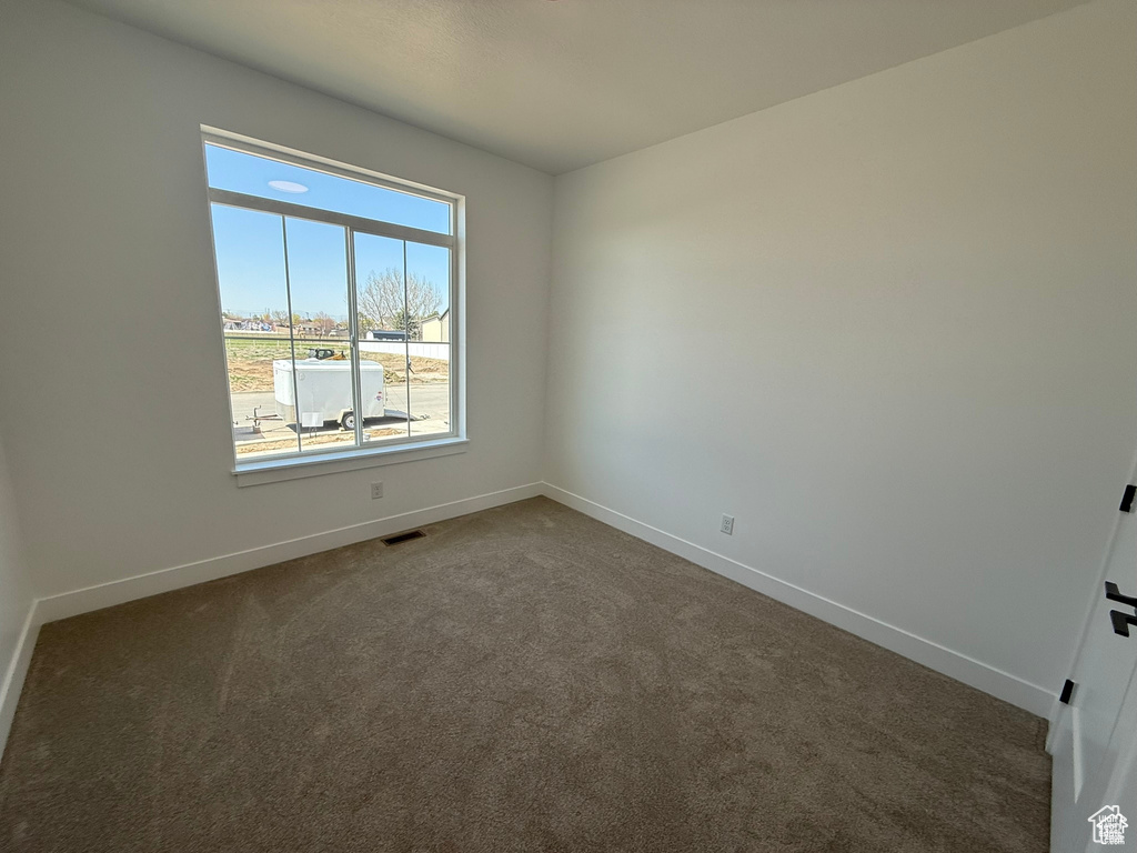 Unfurnished room with visible vents, baseboards, and dark carpet