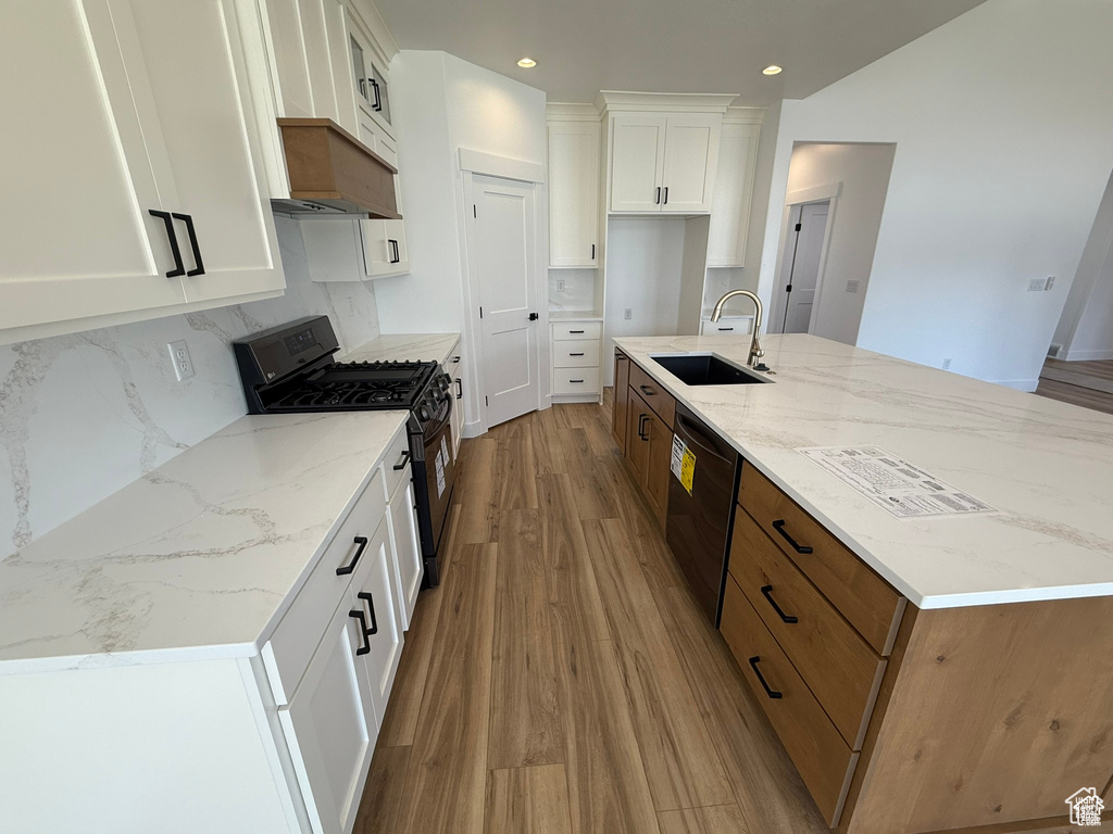 Kitchen featuring light wood-type flooring, white cabinetry, a sink, backsplash, and black appliances