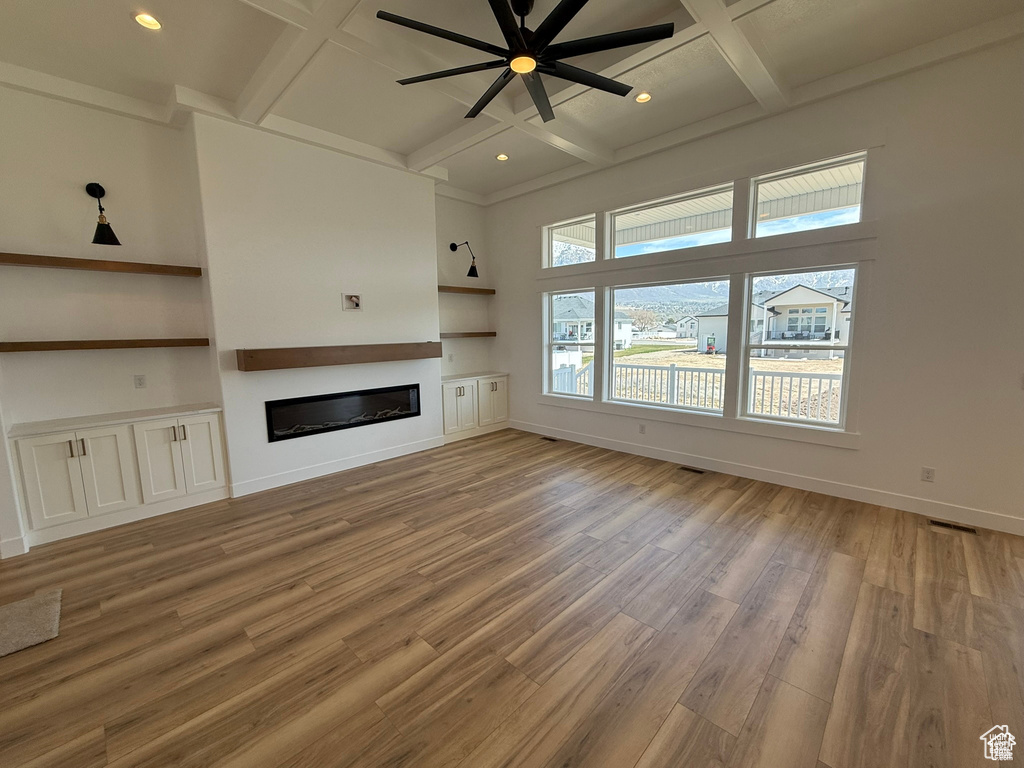 Unfurnished living room featuring ceiling fan, beam ceiling, light wood finished floors, a glass covered fireplace, and coffered ceiling