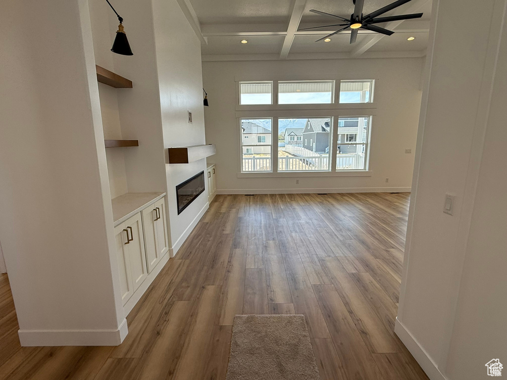 Unfurnished living room featuring ceiling fan, light wood-style floors, a glass covered fireplace, built in features, and coffered ceiling