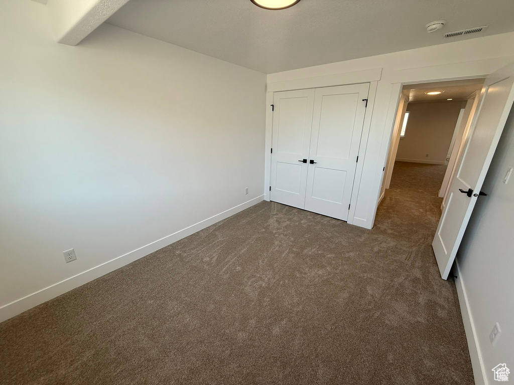 Unfurnished bedroom featuring dark carpet, baseboards, and visible vents