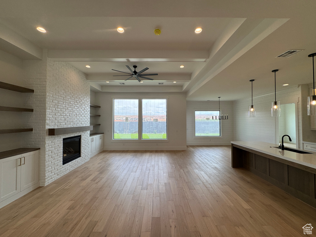 Unfurnished living room featuring ceiling fan, a sink, a brick fireplace, light wood-style flooring, and visible vents