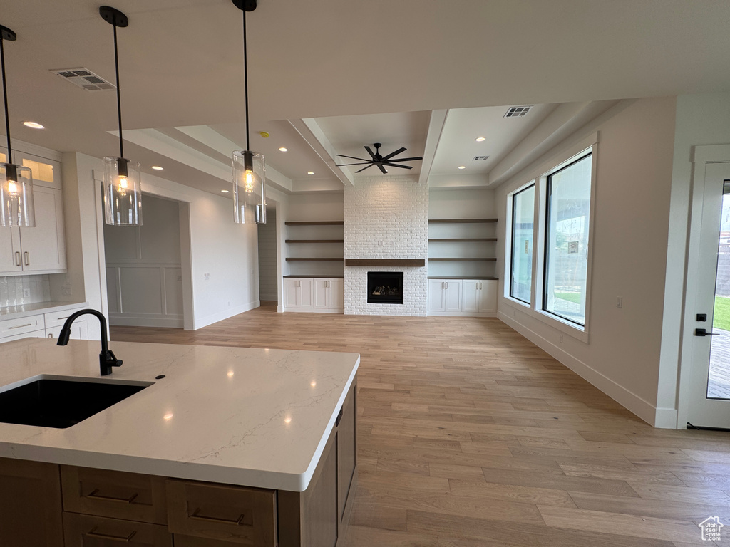 Kitchen featuring a sink, a raised ceiling, light wood-style flooring, baseboards, and visible vents