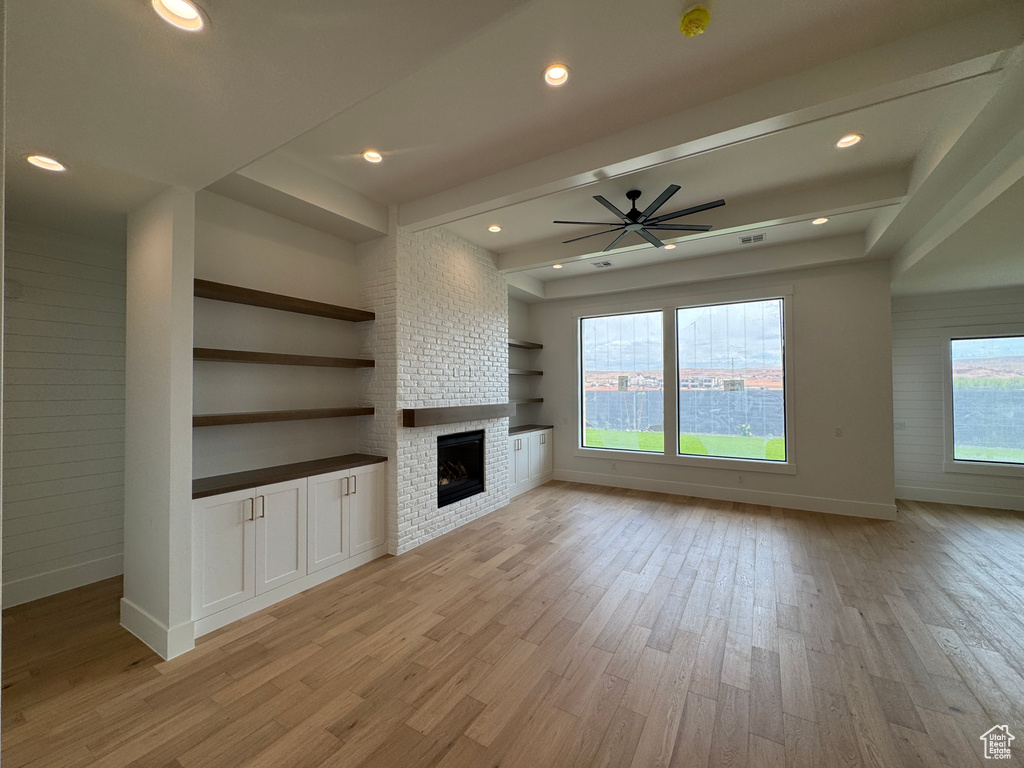 Unfurnished living room featuring baseboards, ceiling fan, a large fireplace, and light wood-style flooring