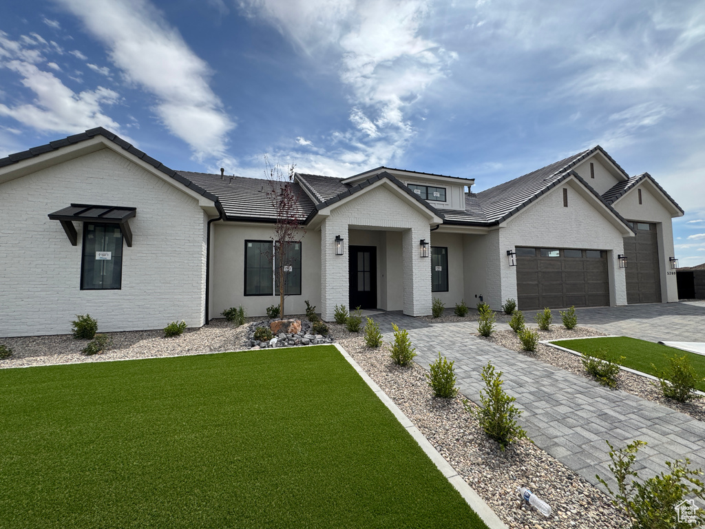 View of front of home featuring brick siding, decorative driveway, a front yard, and a garage