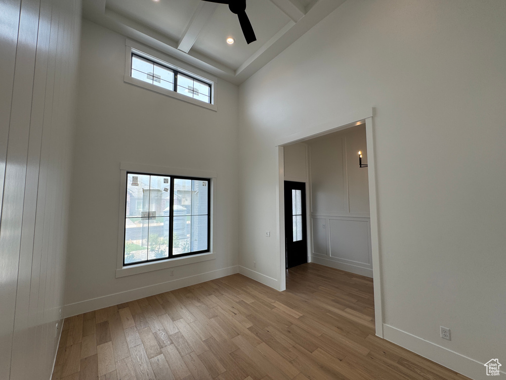 Empty room with ceiling fan, a towering ceiling, light wood-type flooring, beam ceiling, and baseboards