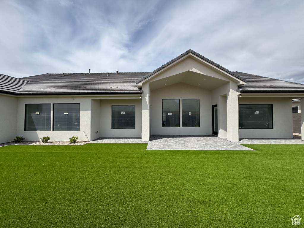 Rear view of property featuring a lawn, a patio area, and stucco siding