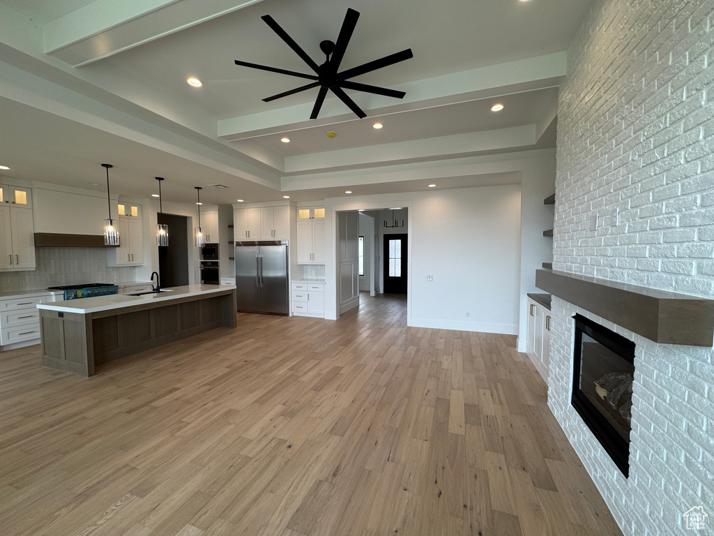 Kitchen featuring appliances with stainless steel finishes, a large island with sink, light wood-type flooring, light countertops, and open floor plan
