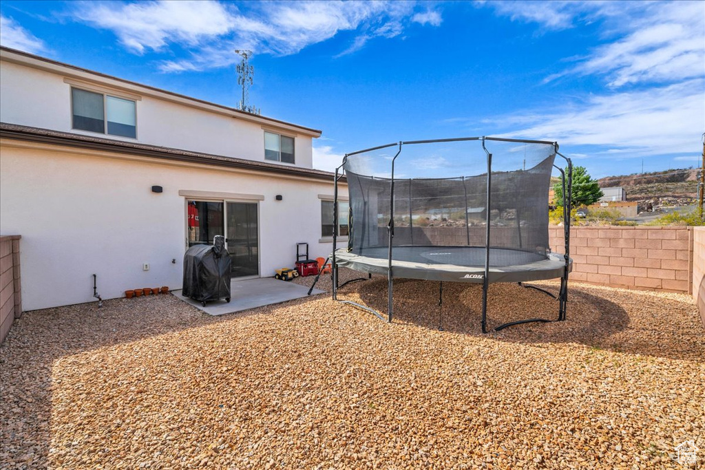 Back of property with a patio, a fenced backyard, a trampoline, and stucco siding