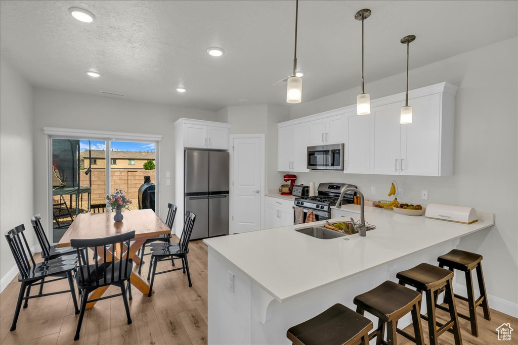 Kitchen with a sink, light wood finished floors, stainless steel appliances, baseboards, and a peninsula