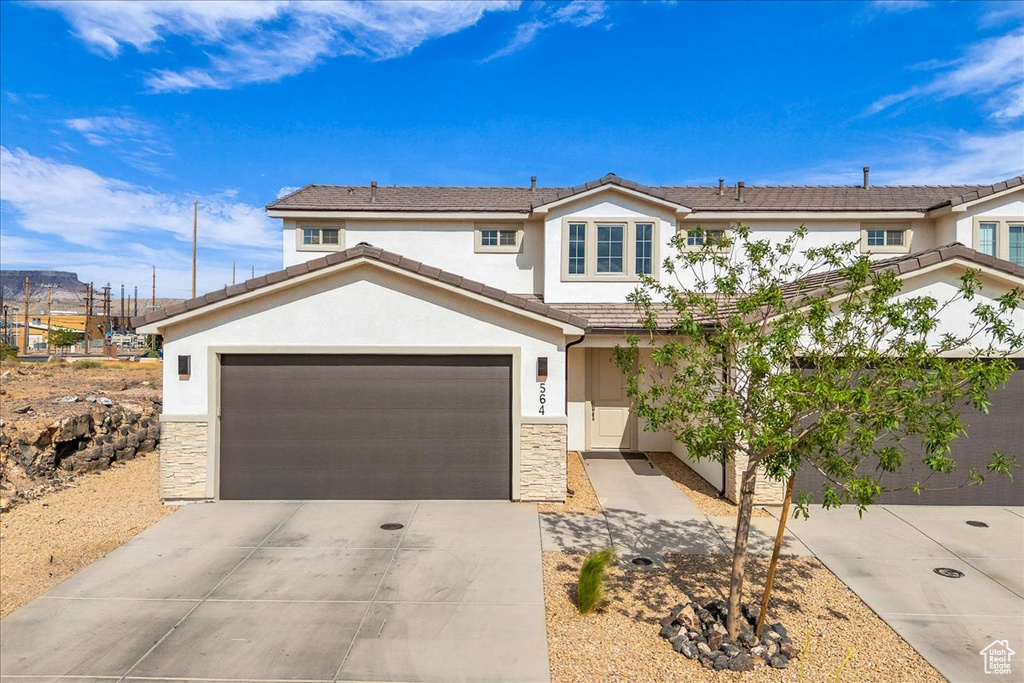 Traditional home with a garage, stucco siding, driveway, and stone siding
