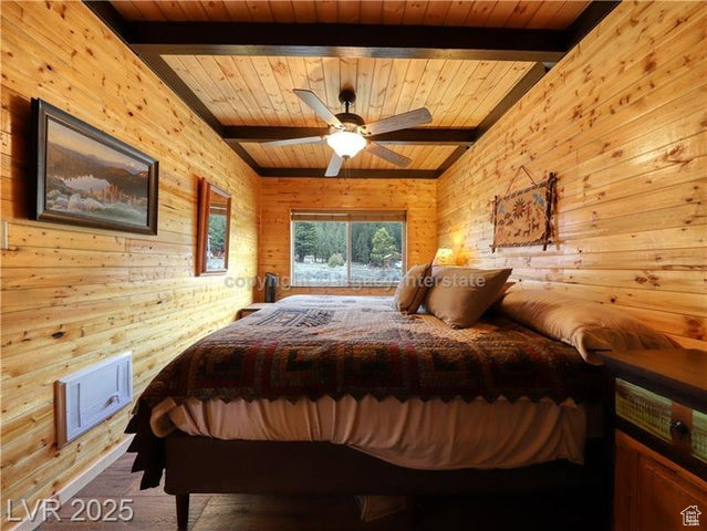 Bedroom featuring wood finished floors, beamed ceiling, ceiling fan, wooden walls, and wooden ceiling