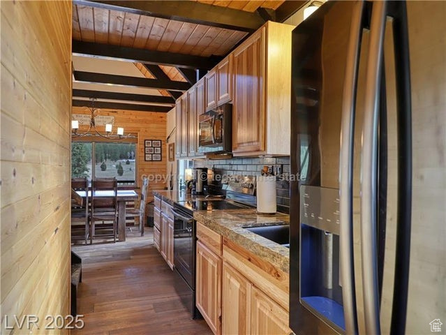 Kitchen featuring dark wood finished floors, wood walls, beam ceiling, fridge with ice dispenser, and black range with electric cooktop