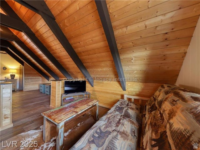 Bedroom with wooden walls, wood ceiling, vaulted ceiling with beams, and wood finished floors