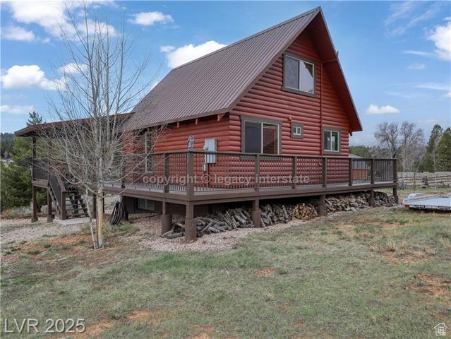 Back of house with a lawn, log veneer siding, a deck, and metal roof