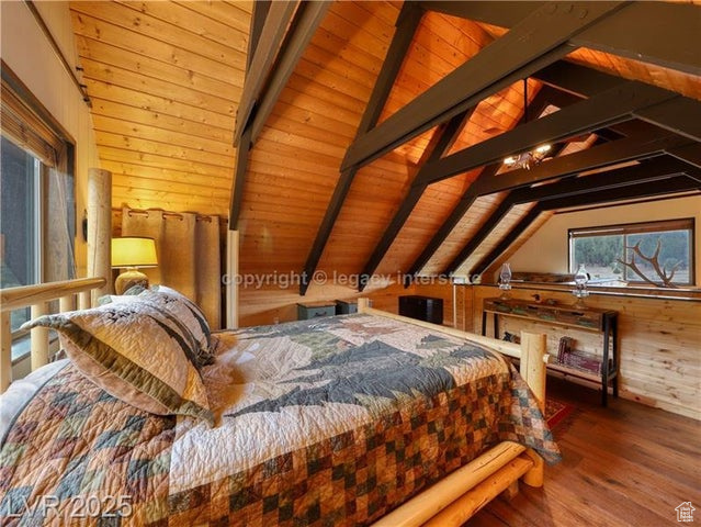 Bedroom featuring lofted ceiling with beams, wood finished floors, wooden walls, and wooden ceiling