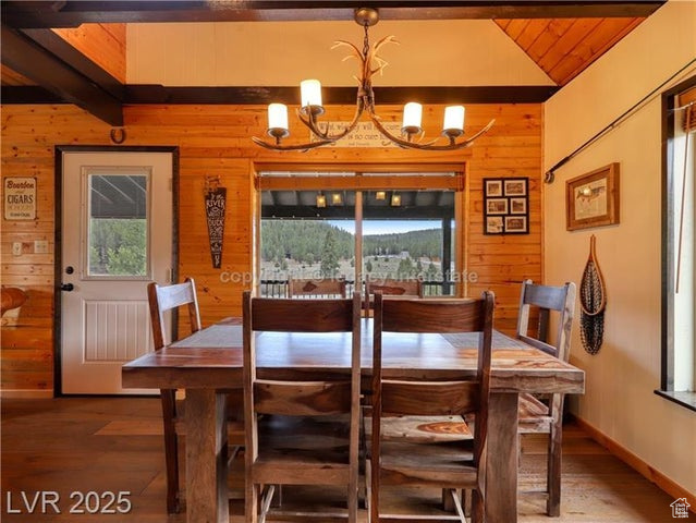 Dining space with wooden walls, a notable chandelier, lofted ceiling with beams, wood finished floors, and wood ceiling