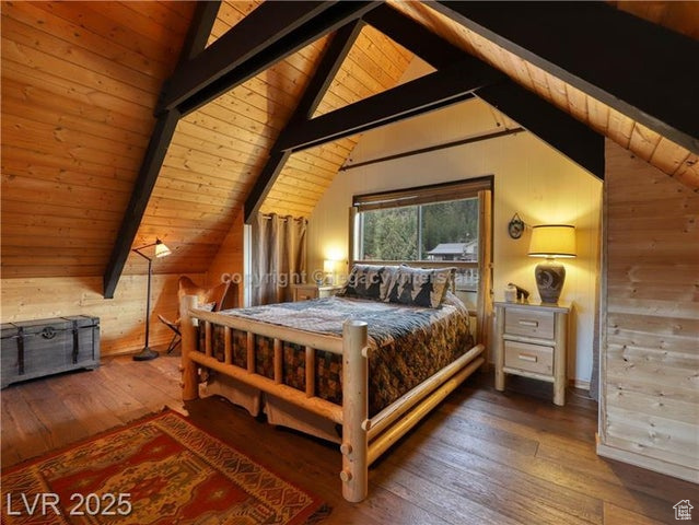 Bedroom featuring wooden walls, wooden ceiling, vaulted ceiling with beams, and hardwood / wood-style floors