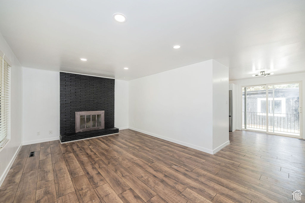 Unfurnished living room featuring baseboards, a brick fireplace, recessed lighting, and wood finished floors
