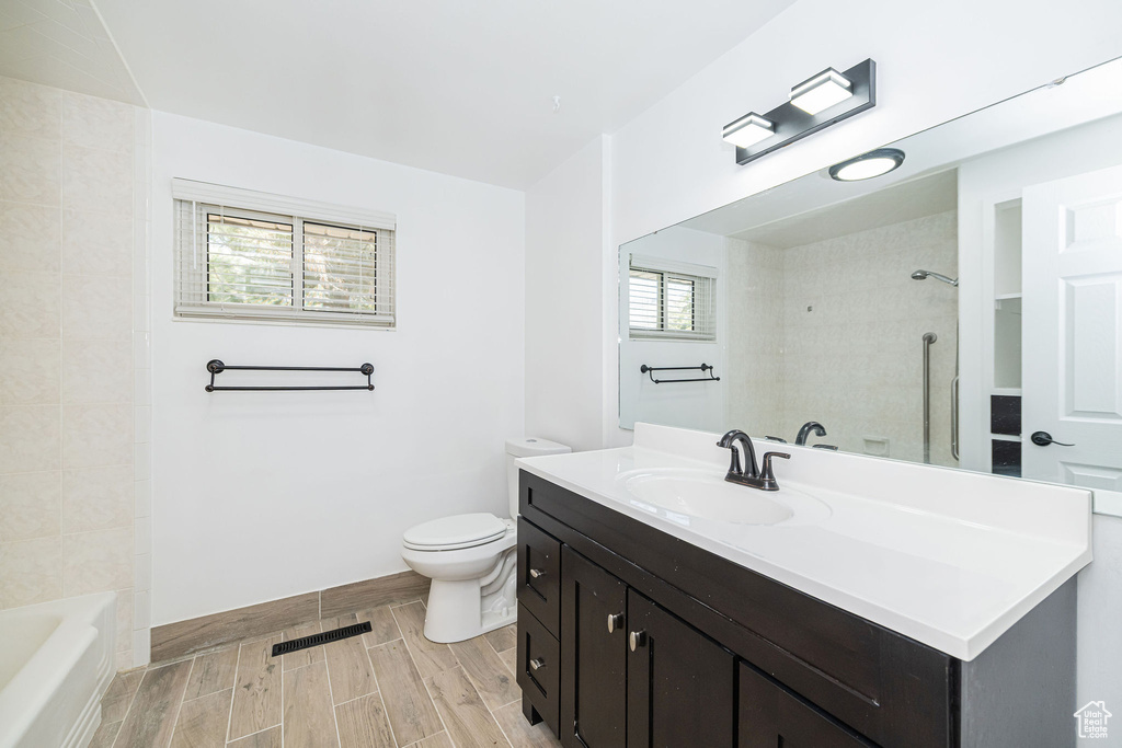 Full bathroom with wood finish floors, vanity, toilet,  shower combination, and visible vents
