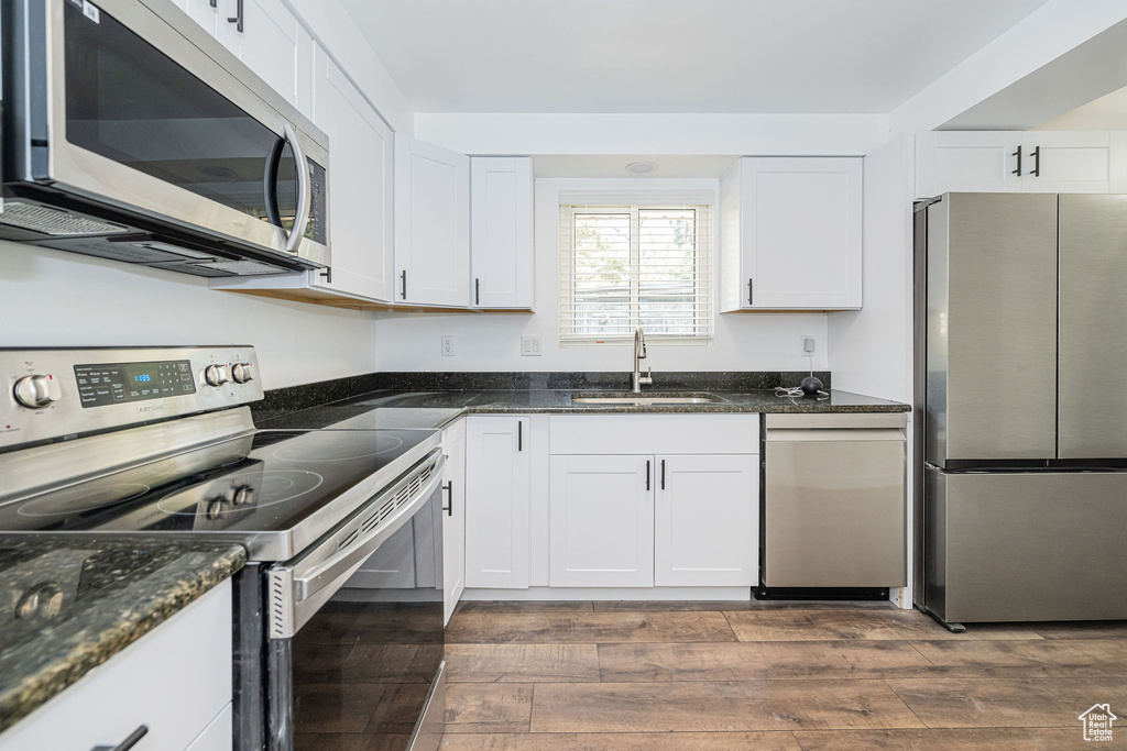 Kitchen with dark wood-style floors, white cabinets, a sink, dark stone countertops, and appliances with stainless steel finishes