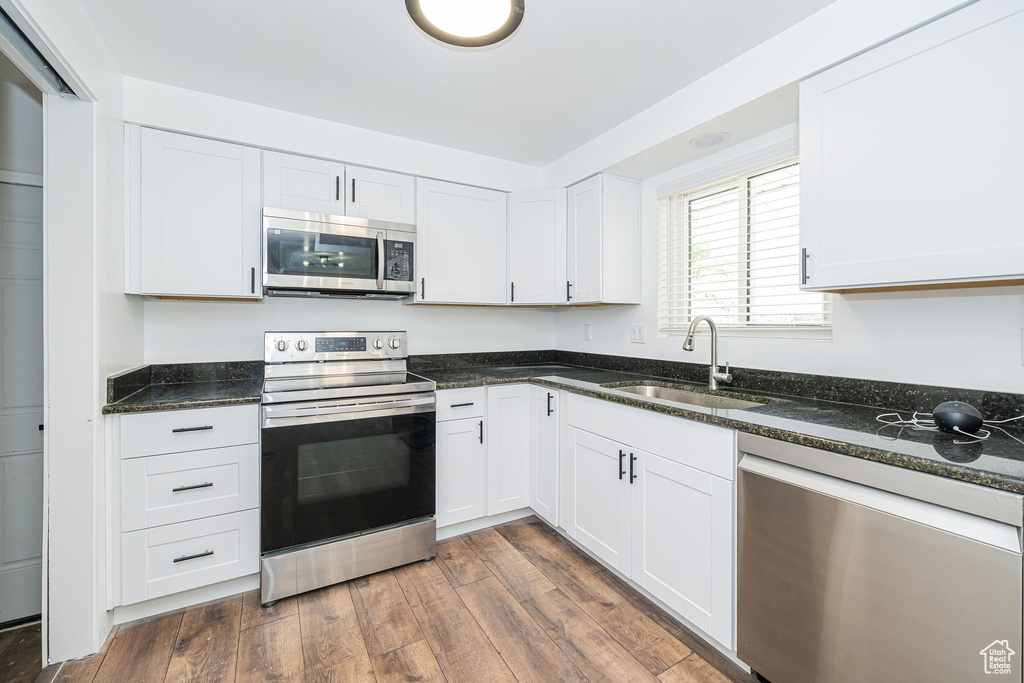 Kitchen featuring dark wood-style flooring, white cabinets, a sink, dark stone countertops, and appliances with stainless steel finishes