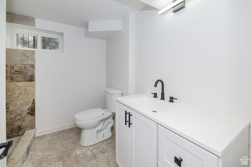 Bathroom with vanity, toilet, stone tile floors, baseboards, and tiled shower