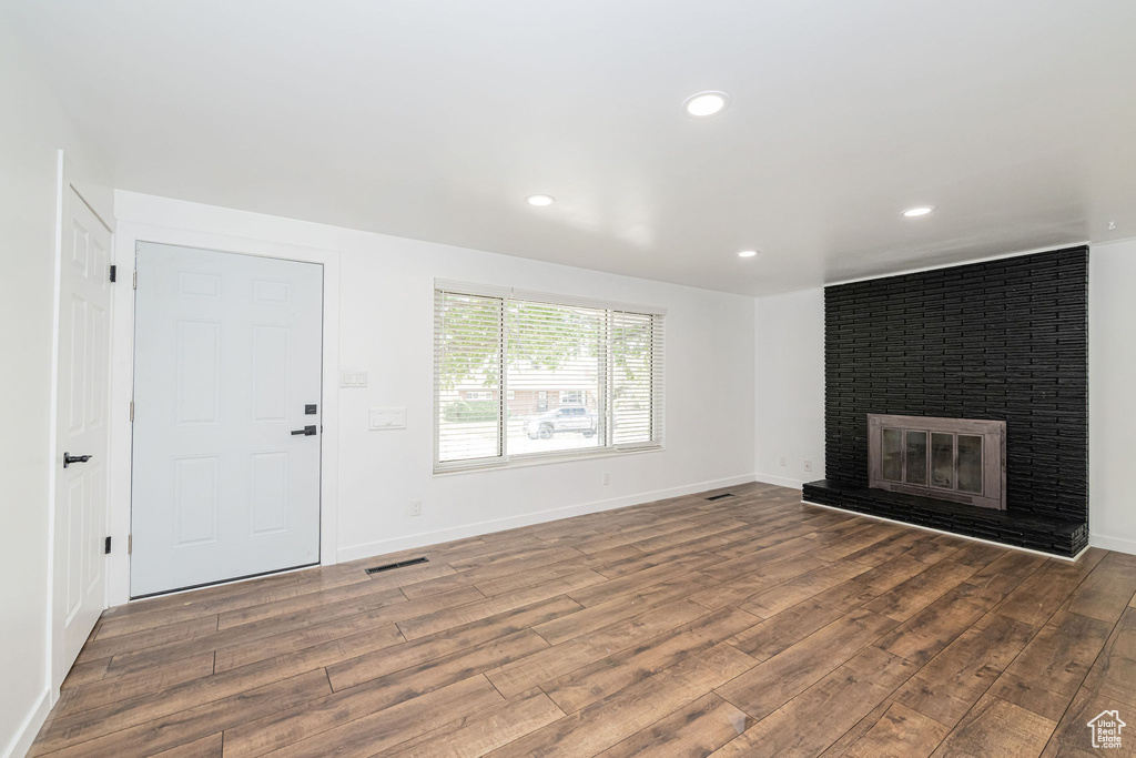 Unfurnished living room with visible vents, baseboards, a brick fireplace, and wood finished floors