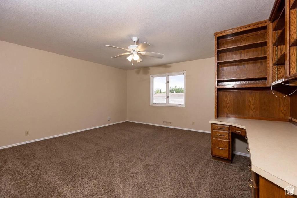 Unfurnished office featuring baseboards, a textured ceiling, ceiling fan, and dark carpet