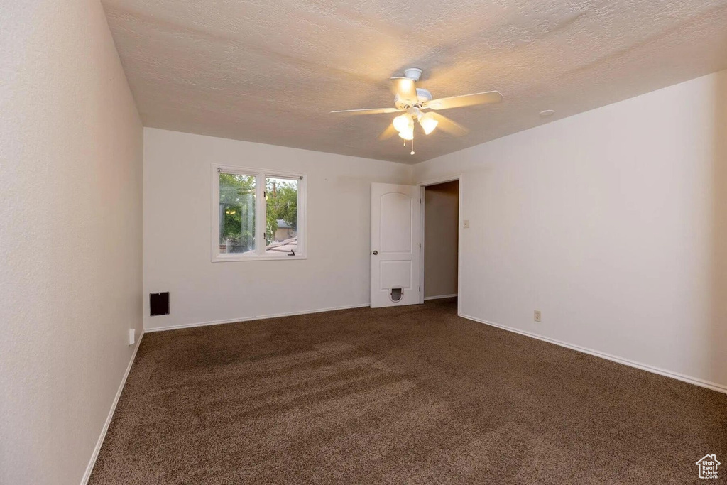 Empty room featuring baseboards, a ceiling fan, a textured ceiling, and dark carpet