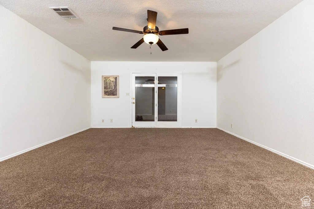 Unfurnished room featuring baseboards, ceiling fan, visible vents, and dark carpet