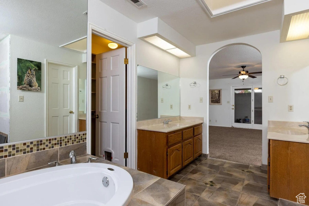 Full bathroom featuring a garden tub, a ceiling fan, a sink, and two vanities