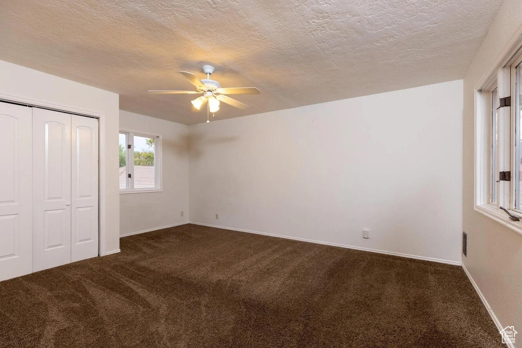Unfurnished bedroom with baseboards, a textured ceiling, dark carpet, and a closet