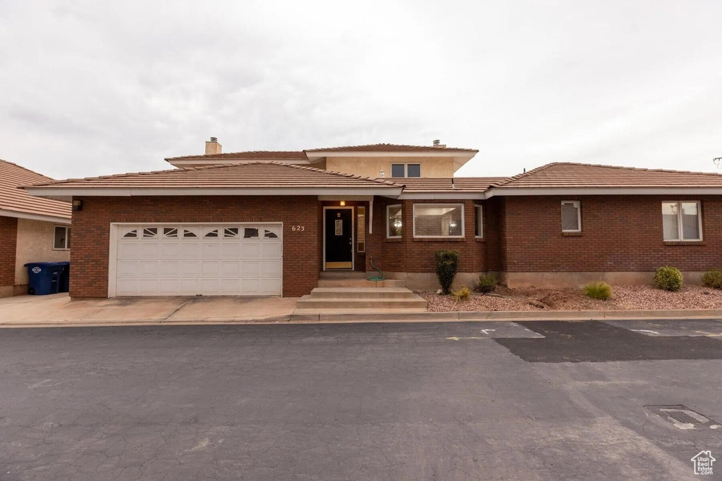 Prairie-style home with a garage, a chimney, and brick siding
