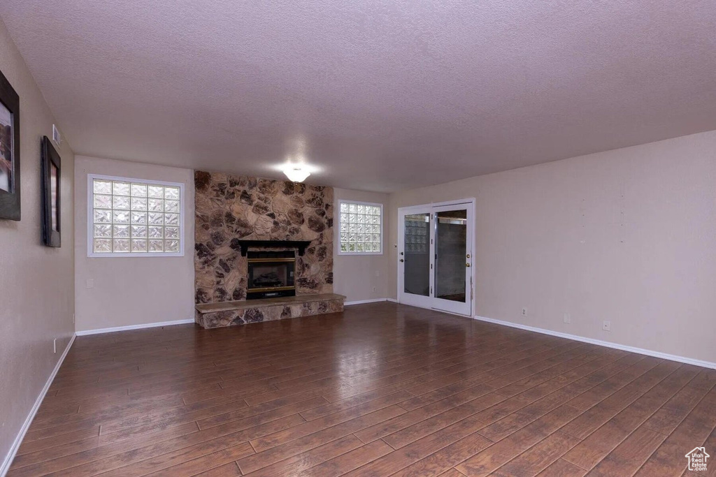 Unfurnished living room featuring a textured ceiling, a stone fireplace, baseboards, and dark wood-type flooring