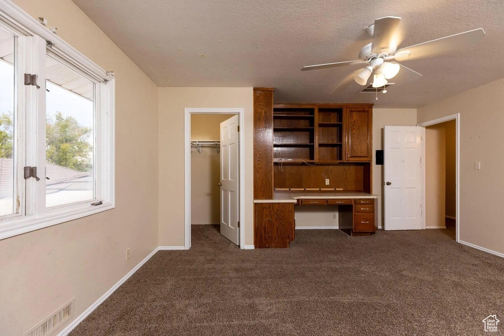 Unfurnished bedroom with a walk in closet, visible vents, built in study area, baseboards, and dark colored carpet