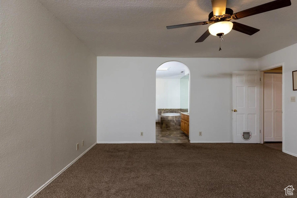 Unfurnished room featuring dark colored carpet, arched walkways, baseboards, and a ceiling fan