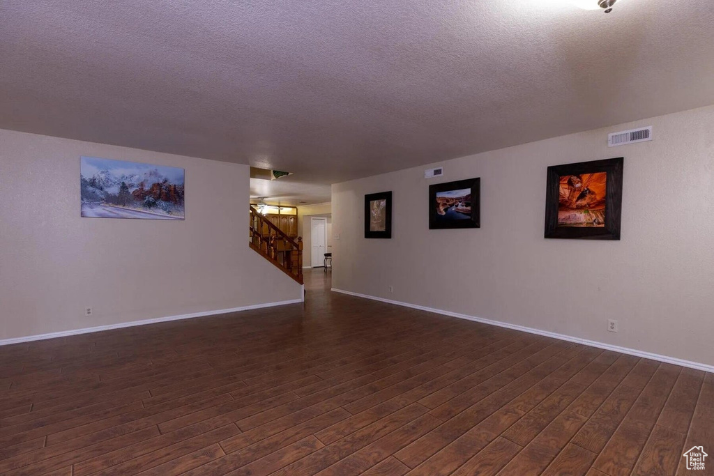 Unfurnished room with dark wood-style flooring, a textured ceiling, visible vents, stairway, and baseboards