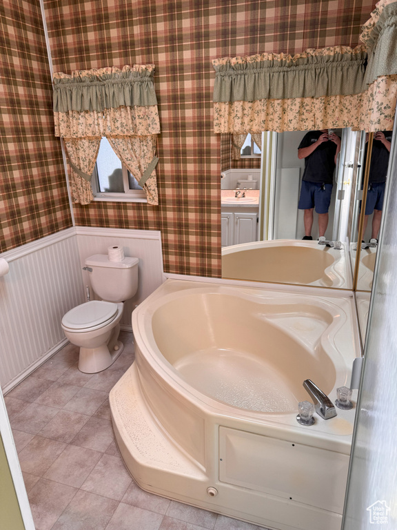 Full bathroom featuring toilet, tile patterned floors, a wainscoted wall, wallpapered walls, and a bath