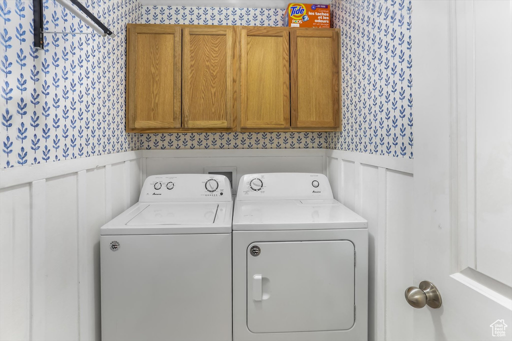 Laundry room featuring wainscoting, wallpapered walls, cabinet space, and washer and dryer