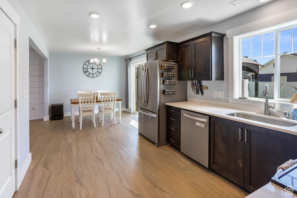 Kitchen with dark brown cabinets, a sink, light countertops, an inviting chandelier, and stainless steel appliances